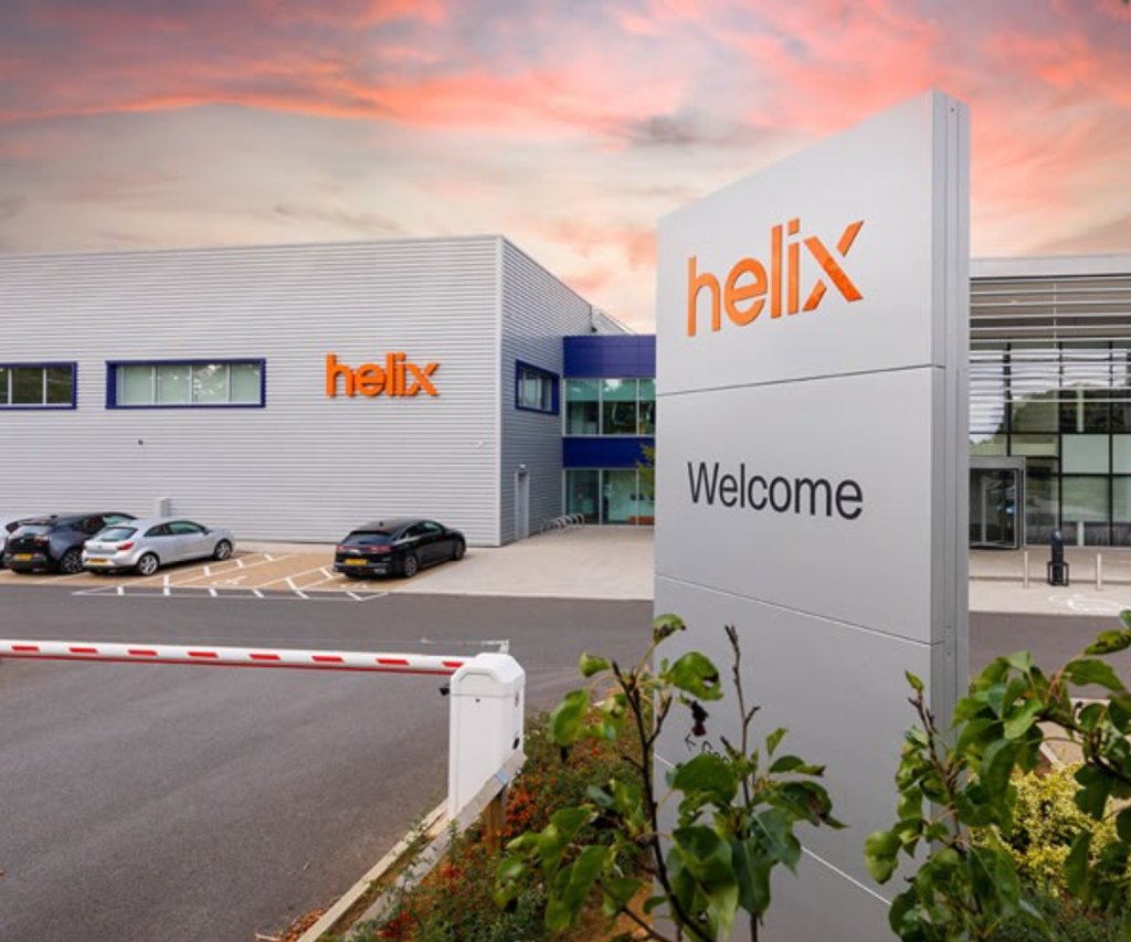 Helix headquarters building with a modern industrial design, featuring a prominent orange logo and ‘Welcome’ signage under a vibrant sunset sky.
